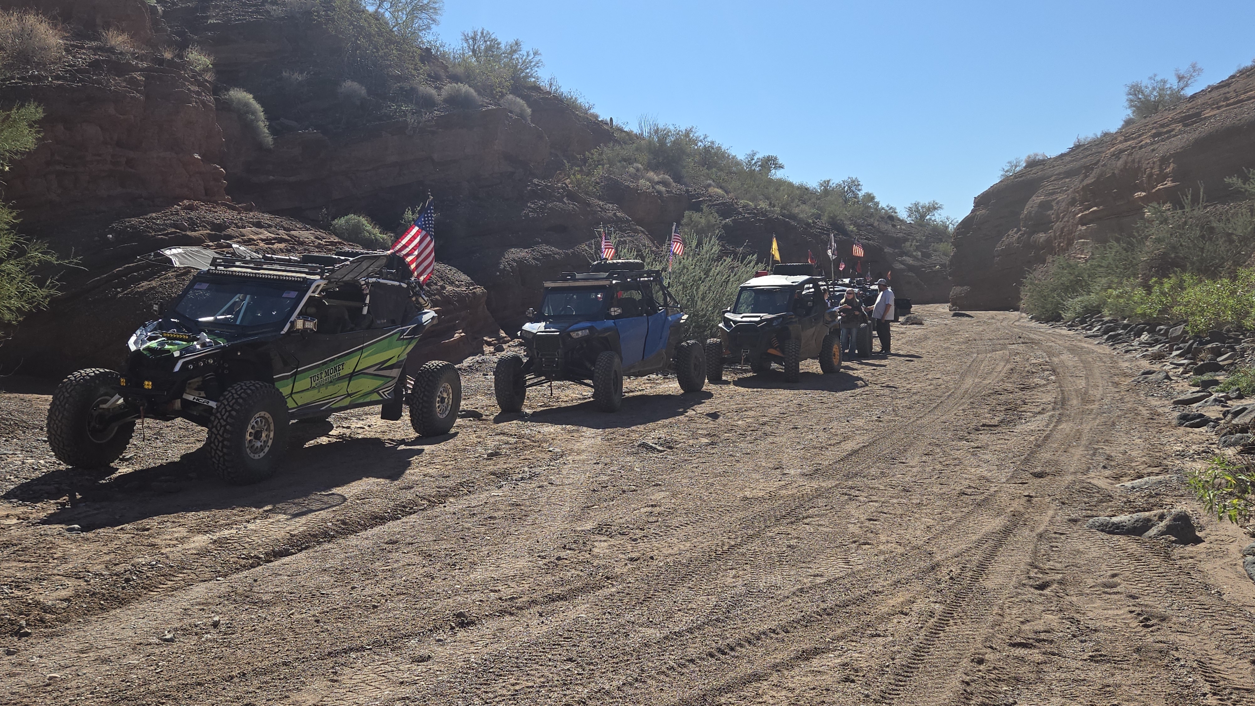 A line of off road vehicles driving up a sandy wash in between canyon walls.