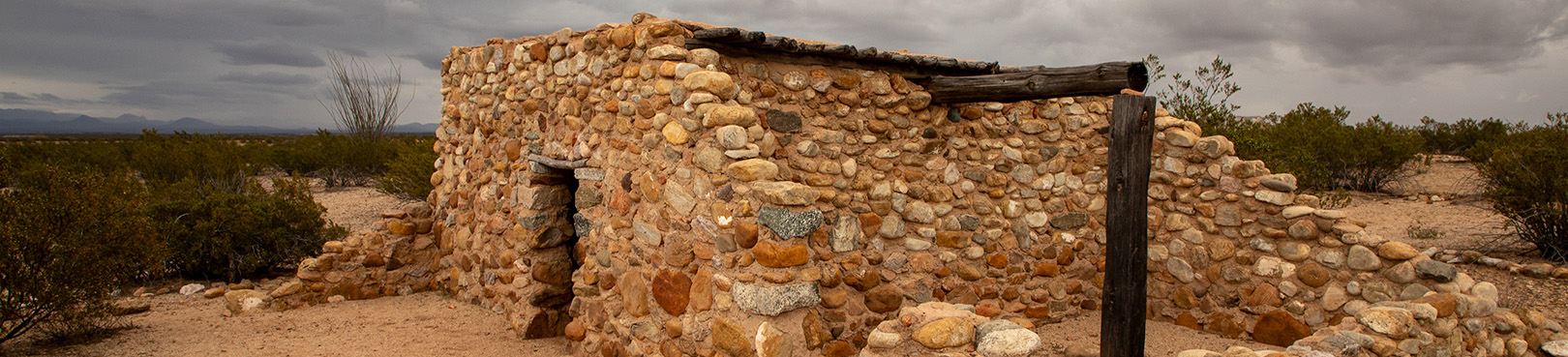 A replica of an ancient rock dwelling sits atop a desert mesa with dark clouds looming in the distance.