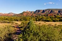 A trail leading through a grassy field with red rock formations in the distance.
